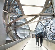 two men are walking down an escalator in a building with large metal sculptures