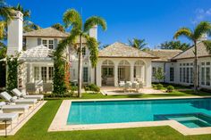 a large white house with a pool in the front yard and palm trees around it