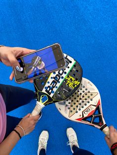 a person holding a cell phone in front of a tennis racket on a blue carpet