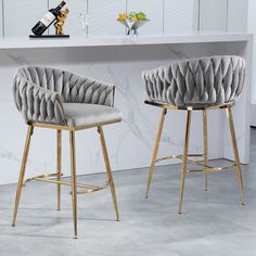 two grey velvet barstools with gold legs in front of a marble countertop