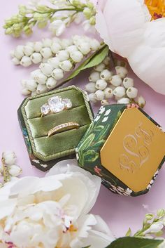 an engagement ring sitting on top of a box surrounded by flowers and peonies