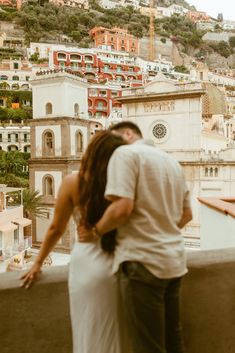 a man and woman standing next to each other on top of a building with buildings in the background