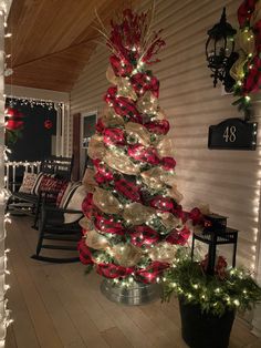 a christmas tree decorated with red and white ribbons on the front porch, lit up by string lights