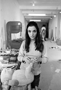 black and white photograph of a woman holding a stuffed animal in a room with other items on the floor