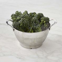 a bunch of broccoli in a colander on a marble counter top,