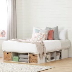 a white bed with drawers underneath it in a room next to a rug and window