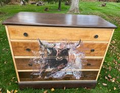 a wooden dresser with an image of a cow painted on the front and bottom drawers