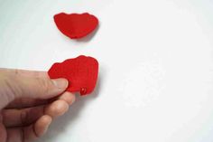 two red hearts are being held in the air by someone's hand on a white surface