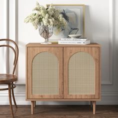 a wooden cabinet sitting next to a chair and vase with flowers on top of it