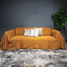 an orange couch with two white pillows on it and a potted plant in the corner