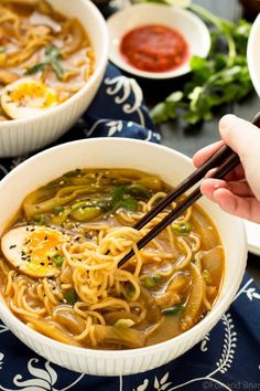 someone is holding chopsticks over a bowl of noodles and vegetable soup with an egg on top