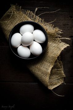 white eggs in a black bowl on a burlap cloth