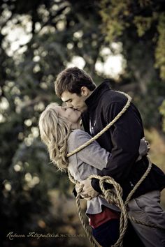 a man and woman kissing each other while tied up to ropes in front of trees