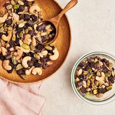 a wooden bowl filled with nuts and raisins next to a glass container full of cashews