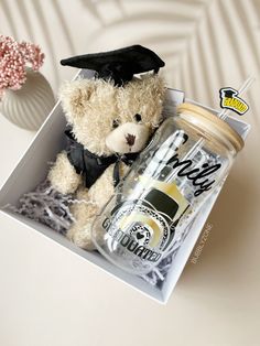 a teddy bear in a graduation cap and gown sits next to a mason jar