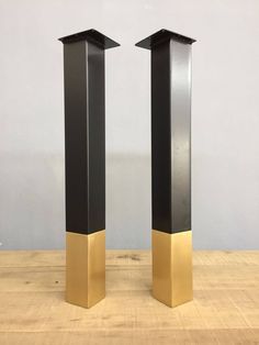 two tall black and gold vases sitting on top of a wooden table next to each other