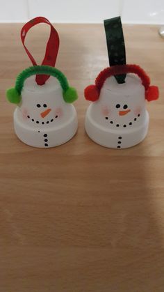 two plastic snowmen with red hats and green hair on top of a wooden table