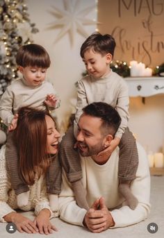 a man, woman and two children laying on the floor in front of a christmas tree