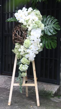 white flowers and greenery are arranged on an easel in front of a black door