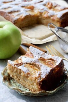 an apple pie with powdered sugar on top sits next to a fork and knife