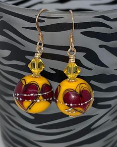 Beautiful lampwork beads in a mustard yellow with burgundy hearts.  They have sterling silver droplets on the outside.  I paired them with gorgeous yellow Swarovski crystals.   They are securely wire wrapped and have bright gold daisy spacers between them.  I suspended them from 14k gold filled ear wires.     Earrings measure 1.5" long Will come gift packed. Follow me on Facebook and Instagram and NYC Fashion Connection for exclusive coupon codes and sneak previews! Yellow Heart-shaped Jewelry For Valentine's Day, Yellow Heart-shaped Jewelry, Yellow Heart Beads Jewelry For Valentine's Day, Yellow Jewelry With Heart Beads For Valentine's Day, Valentine's Day Yellow Jewelry With Heart Beads, Yellow Czech Glass Round Bead Earrings, Yellow Czech Glass Earrings For Gifts, Yellow Heart Beads Jewelry For Gift, Red Heart-shaped Hand Painted Jewelry