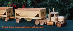 two wooden toy trucks are sitting on a green surface with trees in the background and bushes behind them