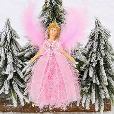 a pink fairy doll sitting on top of a wooden bench next to trees covered in snow