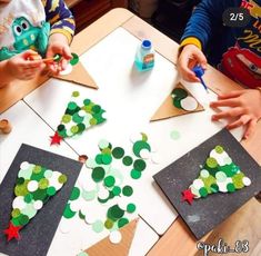 two children are making christmas trees out of construction paper on the table with glue and scissors