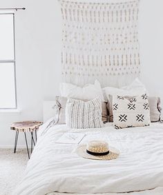 a bed with white sheets and pillows in a bedroom next to a large window that has a hat on top of it