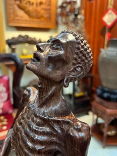 a wooden statue of a woman with her eyes closed in front of a chair and other antiques