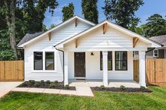 a small white house with a wooden fence around it's front yard and trees in the background