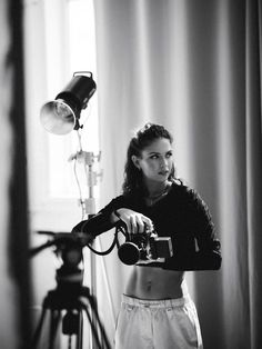 a black and white photo of a woman holding a camera in front of a light