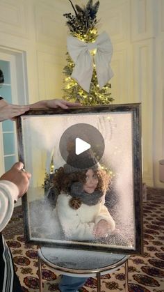 a woman holding up a framed photo in front of a christmas tree with snow on it