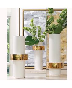 three white vases with gold rims and plants in front of a windowsill