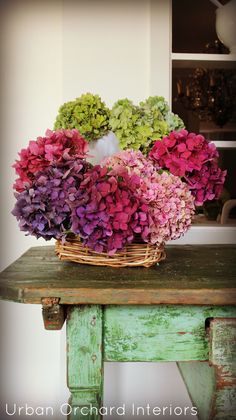 a basket filled with purple and green flowers on top of a wooden table next to a window