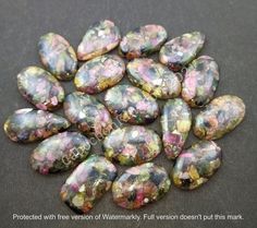 some very pretty colorful rocks on a black surface with watercolor paint all over them