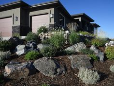 a house is shown with large rocks in the foreground and bushes on the other side