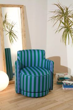 a blue and green striped chair sitting in front of a mirror next to a plant