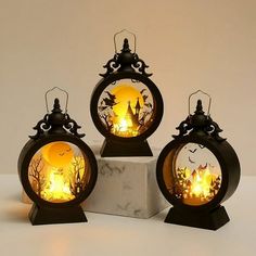 three small lanterns are sitting on top of a marble block and one is lit up with yellow light