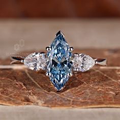 a blue diamond ring with three pear shaped diamonds on it's sides, sitting on top of a leaf