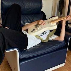 a person laying on a chair with a guitar in their lap and one foot up