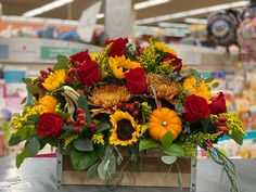 a wooden box filled with red and yellow flowers on top of a table in a store