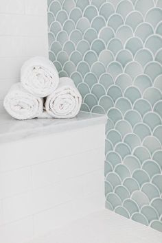 towels stacked on the edge of a bathtub in front of a wall with scalloped tiles