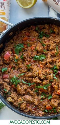 a large pan filled with meat and vegetables next to some lemon wedges on a table