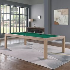 a pool table in the middle of a living room with wood flooring and large windows