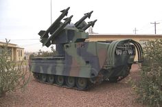 an army tank with missiles on it is parked in the gravel near some bushes and trees