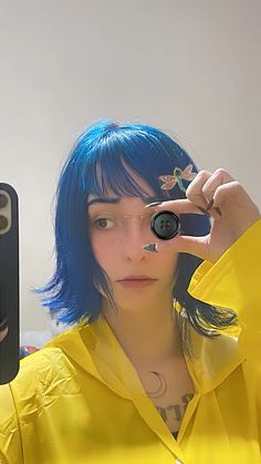 a woman with blue hair and piercings holding up a cell phone to her face