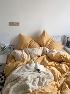 an unmade bed with yellow sheets and blankets on it in a white walled room