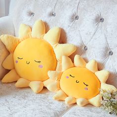 two sun pillows sitting on top of a white couch next to each other with eyes closed