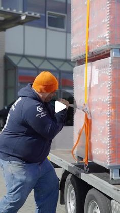 a man in an orange hat and blue jacket is pulling a large box on the back of a truck